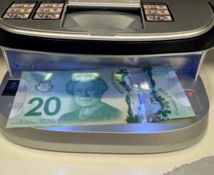 Fake Canadian 10 dollar bill being tested on a counterfeit detection scanner showing UV light verification