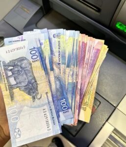 Guy holding stack of fake South African Rand testing counterfeit ZAR notes at ATM for quality verification